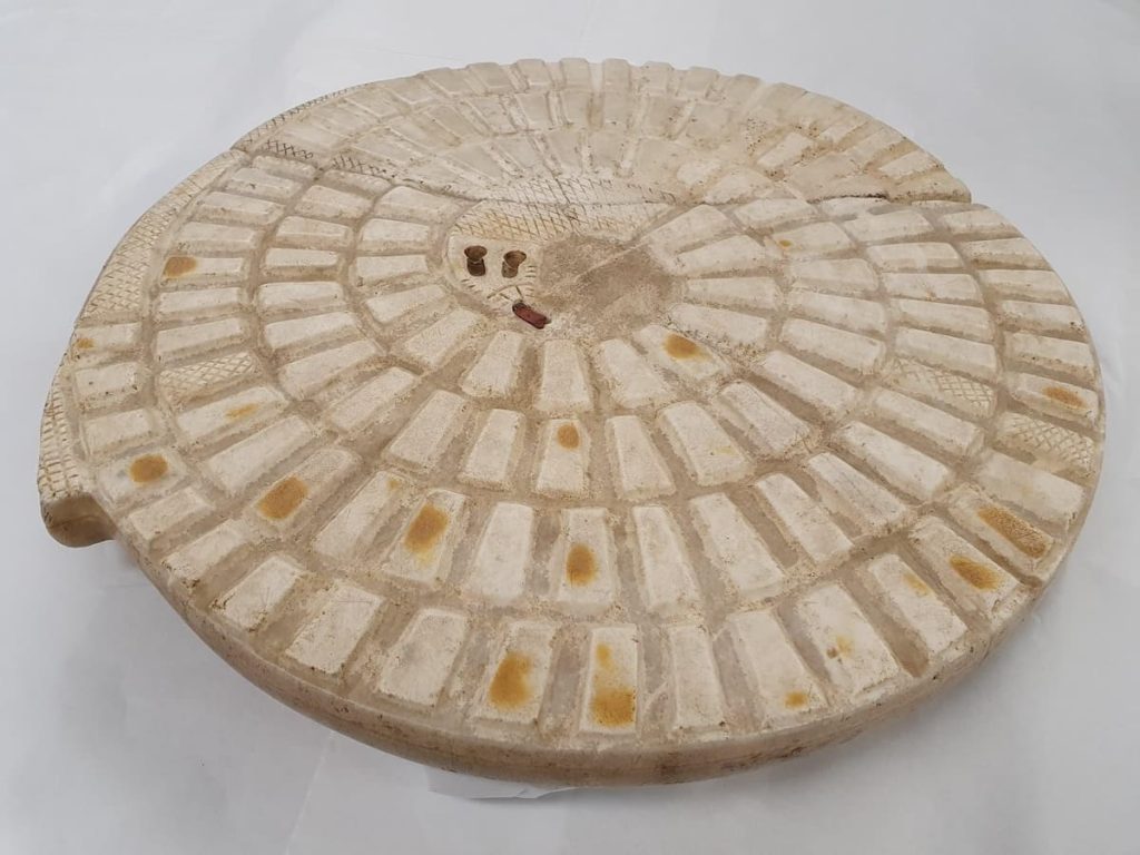 A photograph of an ancient Mehen game board carved in stone with a spiral design and inlaid playing squares.