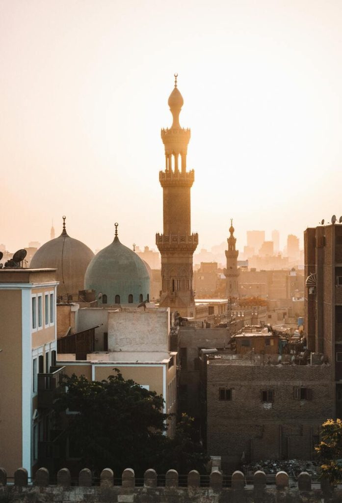 A view of the Cairo skyline at sunset with a prominent minaret and domes in the foreground