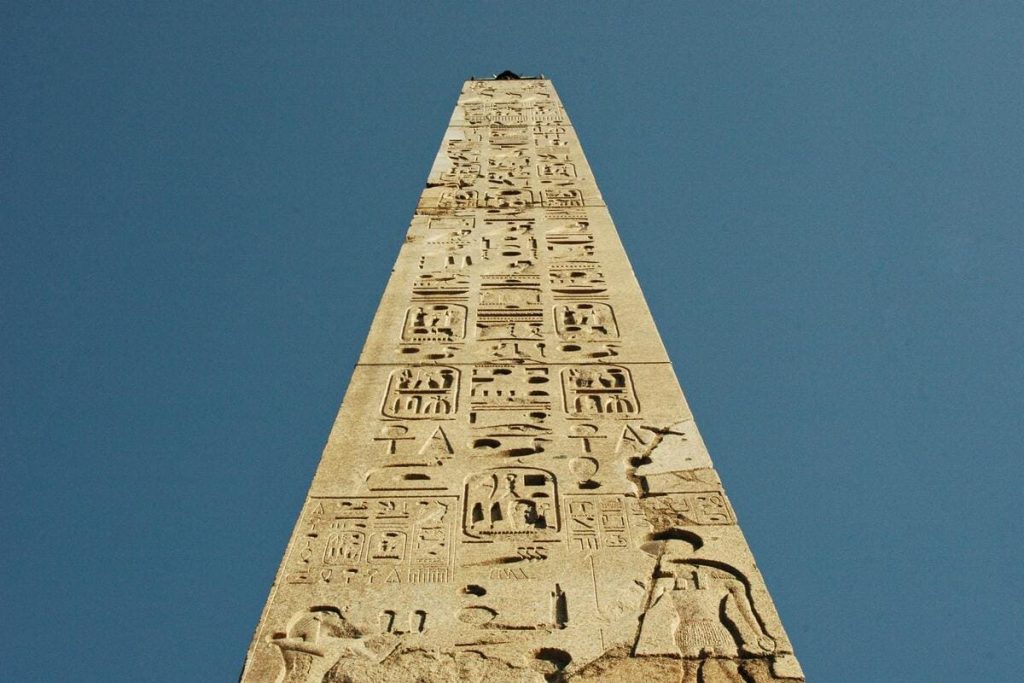 An ancient Egyptian obelisk standing tall against a clear blue sky, adorned with hieroglyphic inscriptions