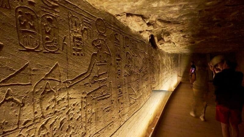 Visitors exploring hieroglyphic carvings inside a tomb in the Valley of the Kings, Luxor, Egypt.