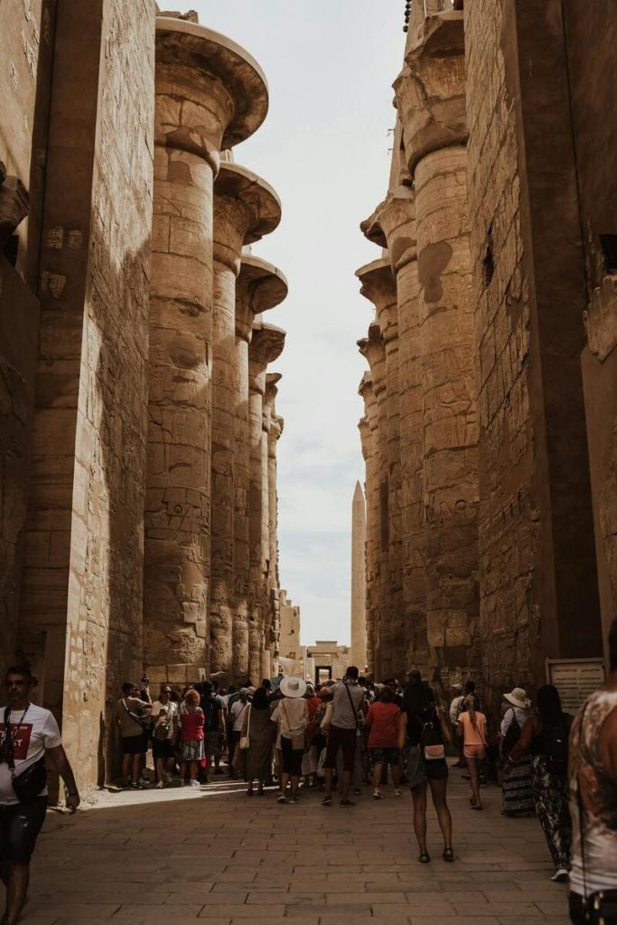 Tourists walking between massive ancient stone columns in the Temple of Karnak, Luxor, Egypt