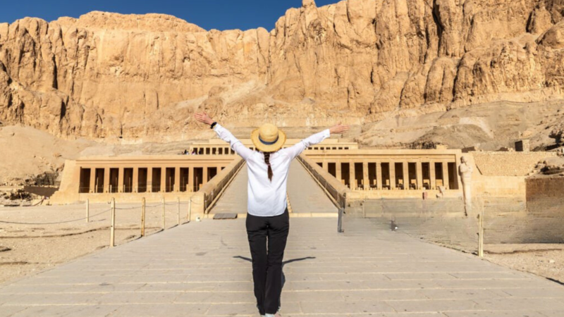 Tourist standing with arms raised in front of Hatshepsut Temple.