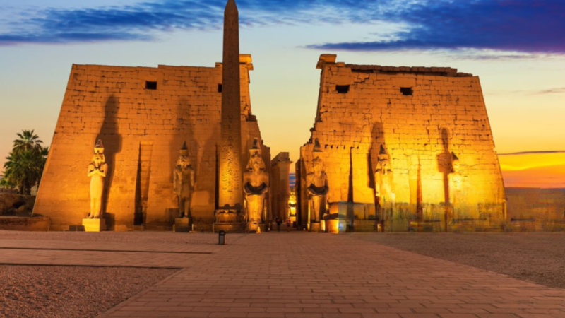 Illuminated Luxor Temple with statues and obelisk at sunset