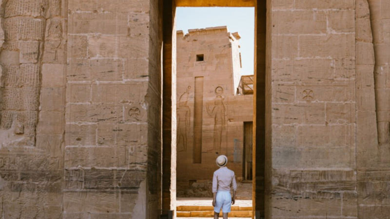 A person standing in awe in front of the grand ancient Egyptian temple with detailed carvings on its stone walls.