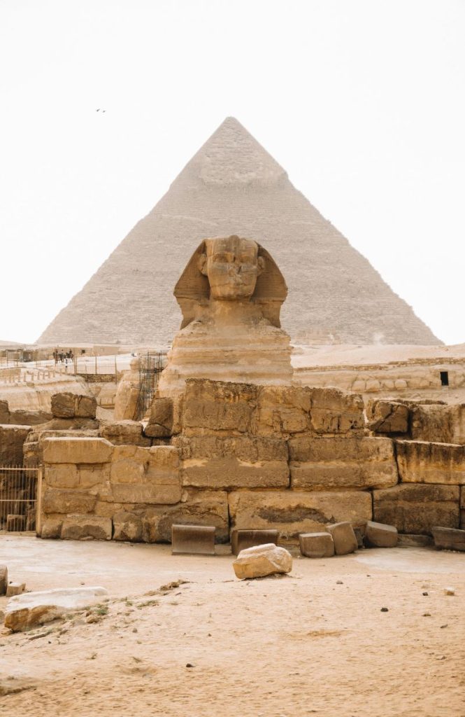 The Great Pyramid of Giza with a clear blue sky and desert landscape, featuring camels and tourists in the foreground