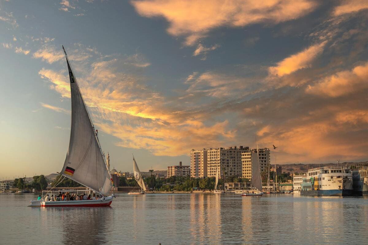 Traditional sailboats on the Nile River at sunset with a city skyline in the background.