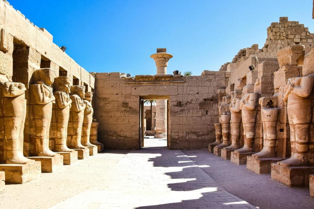 Statues of ancient Egyptian deities and pharaohs in a grand temple, surrounded by towering columns and intricate hieroglyphs