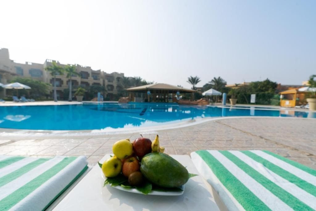 A refreshing fruit platter by the poolside at a luxury resort with a clear blue pool and palm trees in the background.