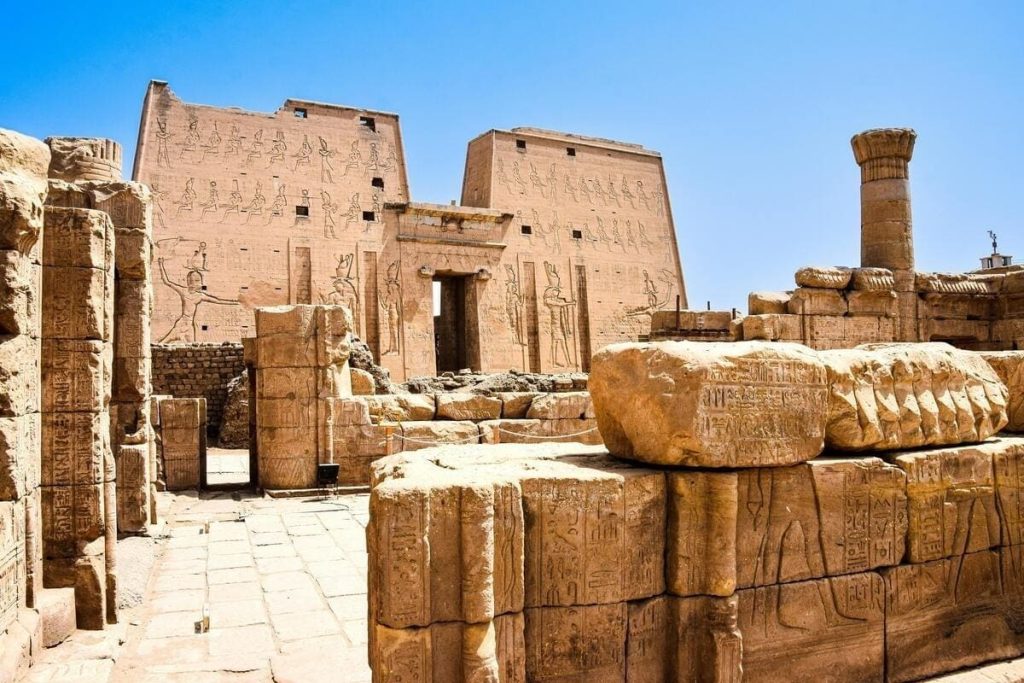 Ruins of an ancient Egyptian temple with tall stone columns and scattered remnants under a clear blue sky