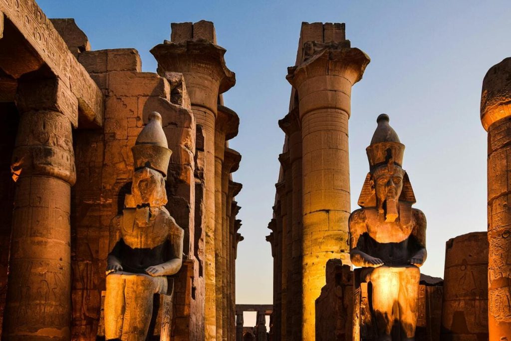 Illuminated statues of pharaohs at Luxor Temple during twilight