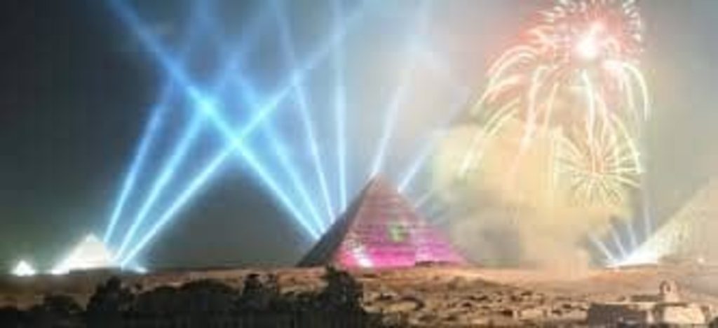 A breathtaking display of fireworks illuminating the night sky above the Pyramids of Giza, with vibrant light beams and colorful explosions.