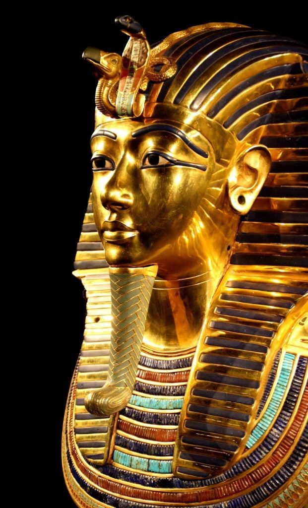 Close-up of the iconic golden mask of Pharaoh Tutankhamun, featuring intricate details like the cobra and vulture headdress, and adorned with stripes of lapis lazuli, carnelian, and turquoise.