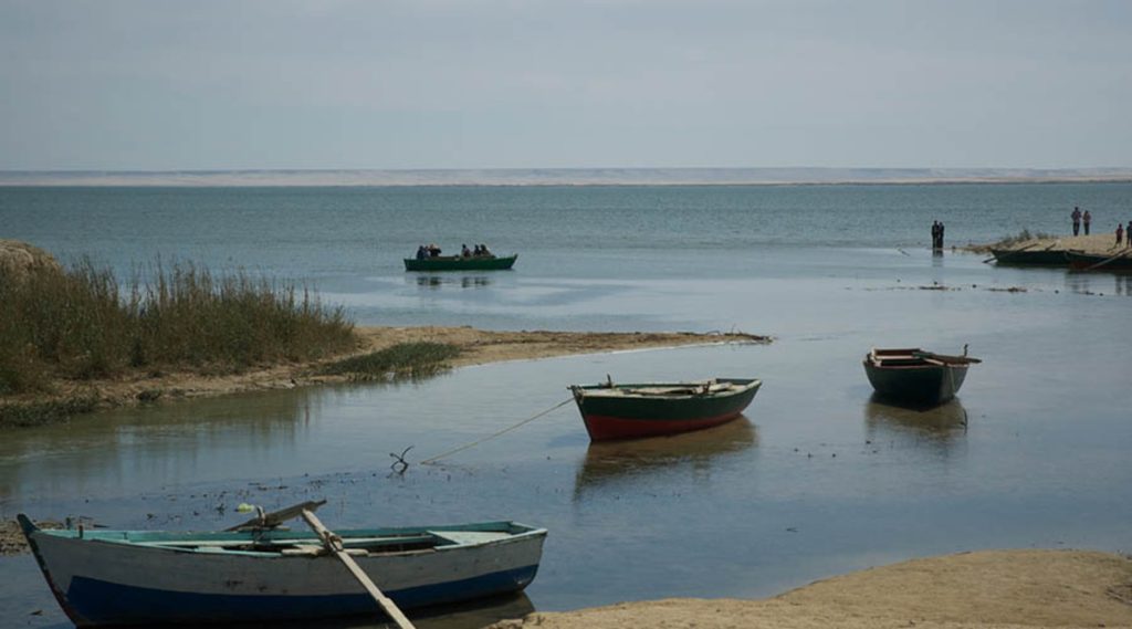 Small boats floating on the serene Qarun Lake in Fayoum, Egypt, with people in the distance and a clear horizon