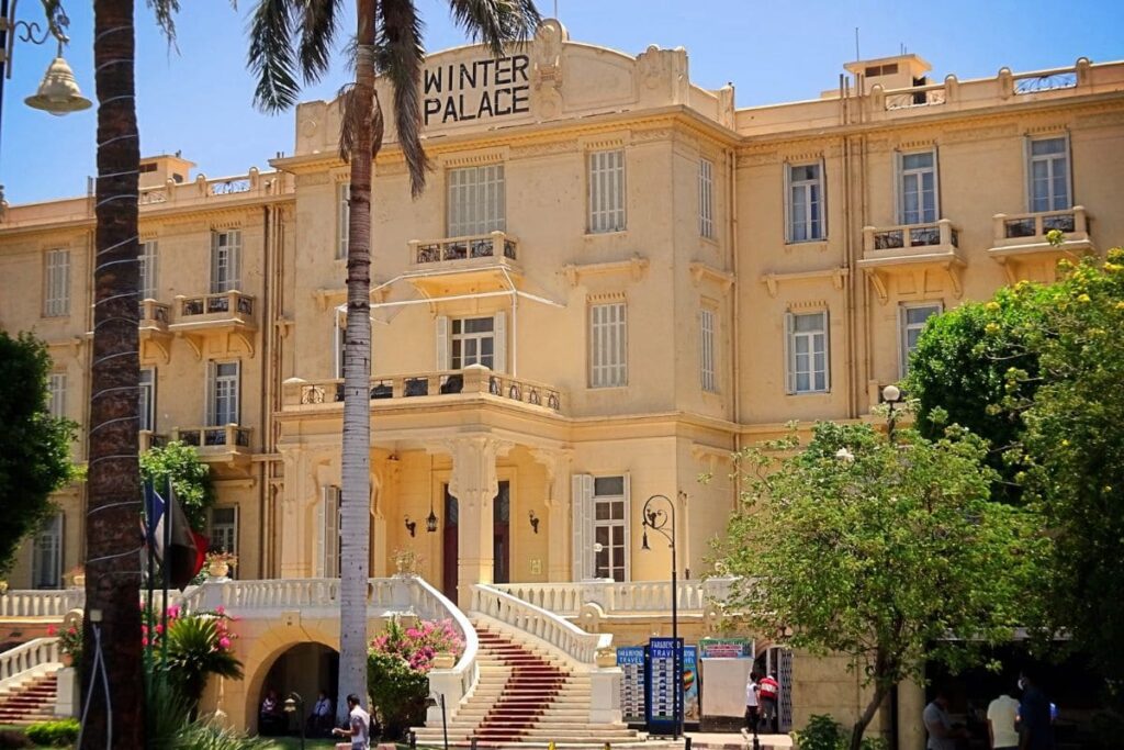 Front view of the historic Winter Palace Hotel in Luxor, Egypt, surrounded by lush greenery under a clear blue sky