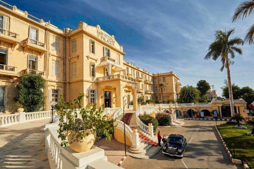 Elegant facade of the Winter Palace Hotel in Luxor, Egypt, featuring classic architecture and surrounded by well-maintained gardens under a sunny sky