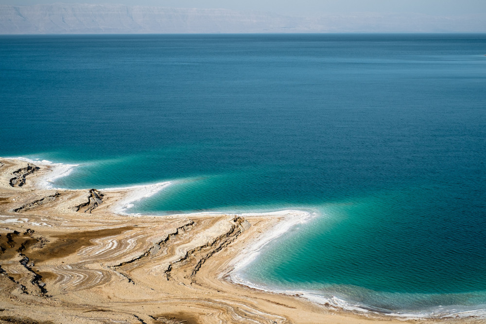 Tranquil view of the Dead Sea with calm, reflective waters, surrounded by rugged hills under a clear sky at the Jordan-Israel border