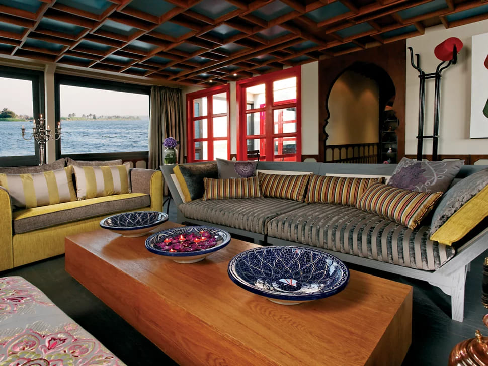 A spacious lounge with comfortable sofas, decorative pillows, and large windows offering views of the Nile River.