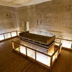 Interior of an ancient Egyptian tomb chamber with a central sarcophagus surrounded by detailed wall inscriptions. Tomb Of General Horemheb