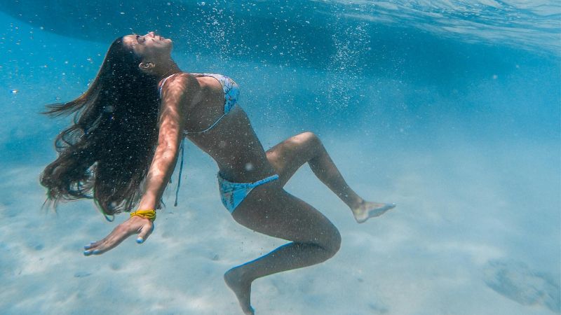 A woman underwater in a serene pose, with her hair flowing freely and bubbles surrounding her in the crystal-clear blue waters