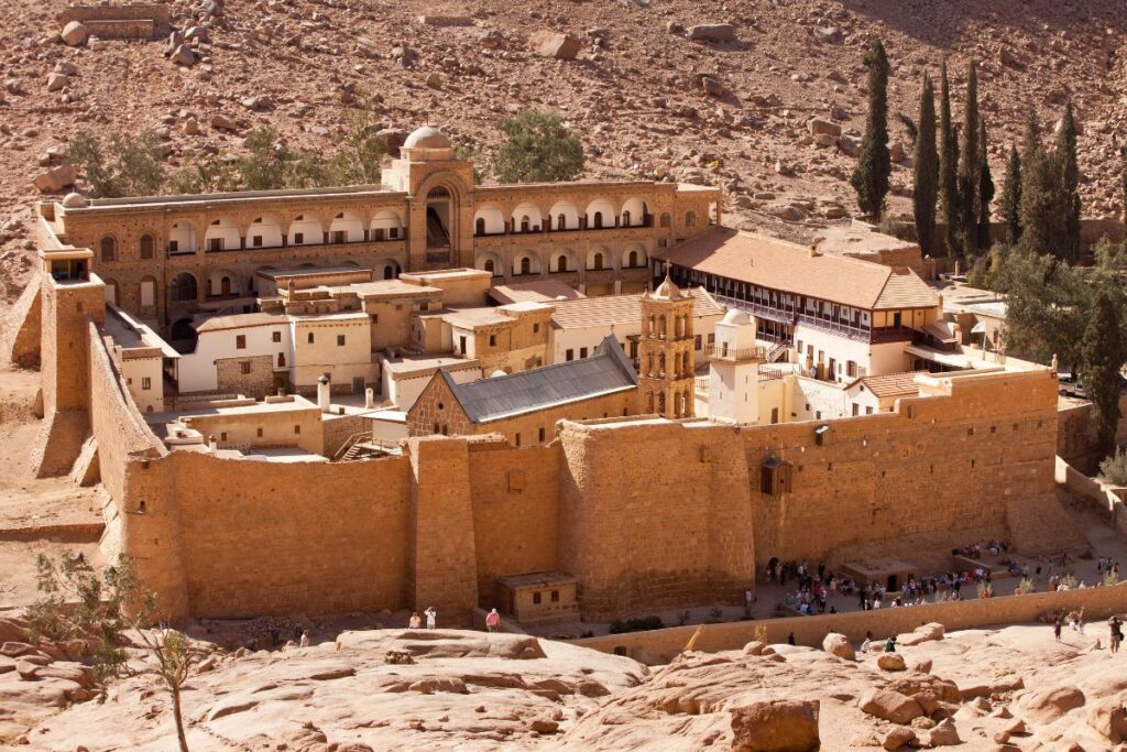 St. Catherine's Monastery at the foot of Mount Sinai, featuring ancient stone architecture surrounded by rugged desert mountains under a clear blue sky