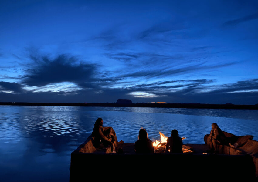 Scenic view of Siwa Lake during a round dinner setup, featuring a tranquil lake surrounded by palm trees, vibrant sunset hues, and cozy seating arrangementsScenic view of Siwa Lake during a round dinner setup, featuring a tranquil lake surrounded by palm trees, vibrant sunset hues, and cozy seating arrangements