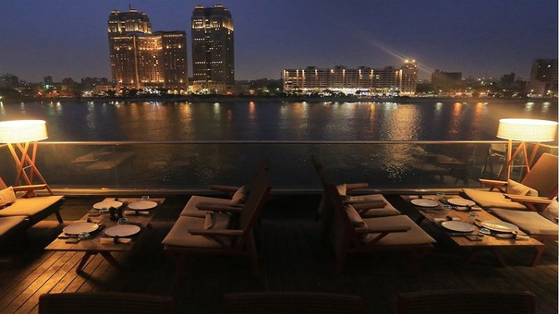 Outdoor dining area overlooking the Nile River at night, with cozy seating and city lights reflecting on the water