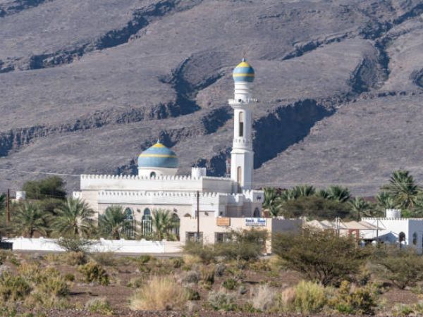 A picturesque mosque with blue domes nestled against a rocky desert backdrop