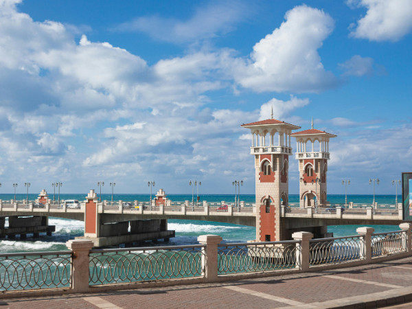 A stunning view of the Alexandria waterfront, featuring a clear blue sky, historic architecture, and a serene sea