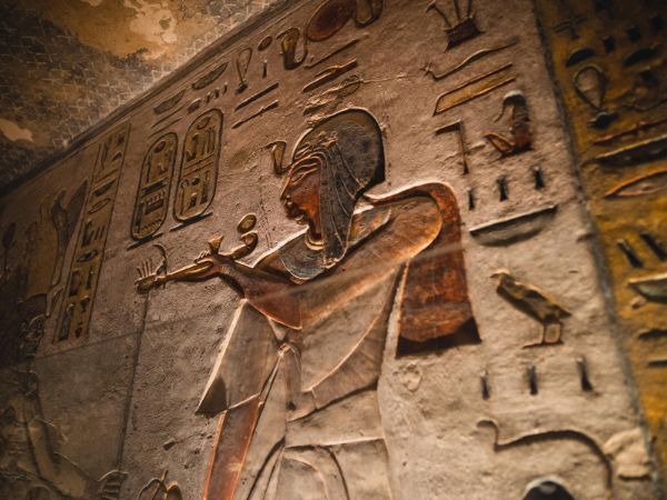 Intricate ancient Egyptian wall carvings depicting pharaohs and deities, etched into stone and illuminated by soft light