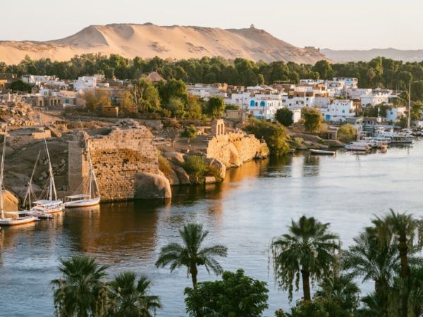 The serene riverside charm of Aswan, featuring traditional felucca boats sailing along the Nile River with lush greenery and scenic views