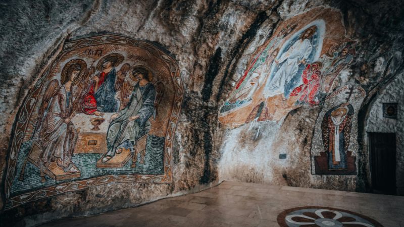 Religious murals painted on a rocky cave wall, depicting biblical scenes with vibrant colors