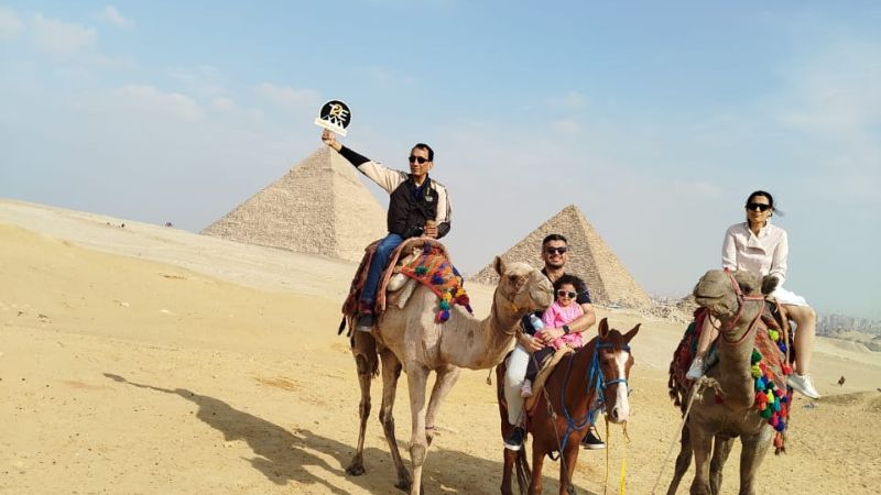 Tourists riding camels with the Great Pyramids of Giza in the background