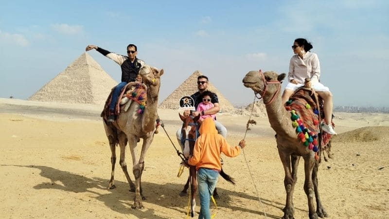 Tourists riding camels in front of the Great Pyramids of Giza on a sunny day