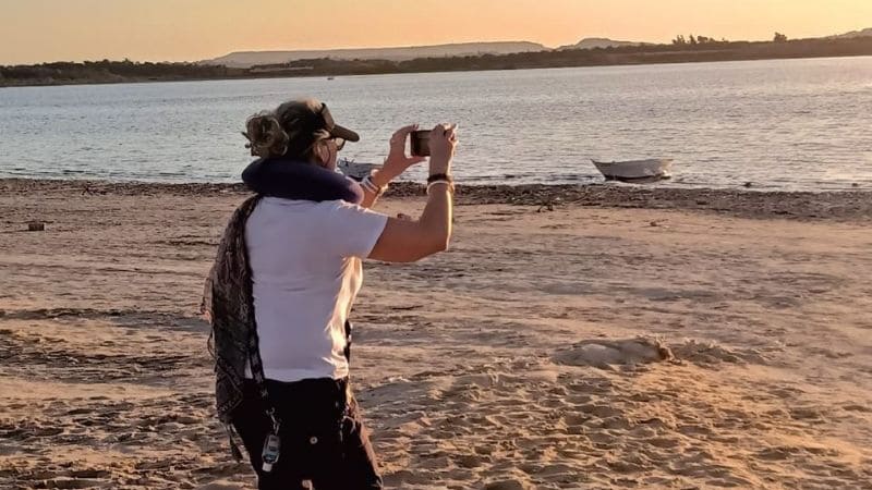 A tourist photographing a serene lakeshore at sunset in Egypt