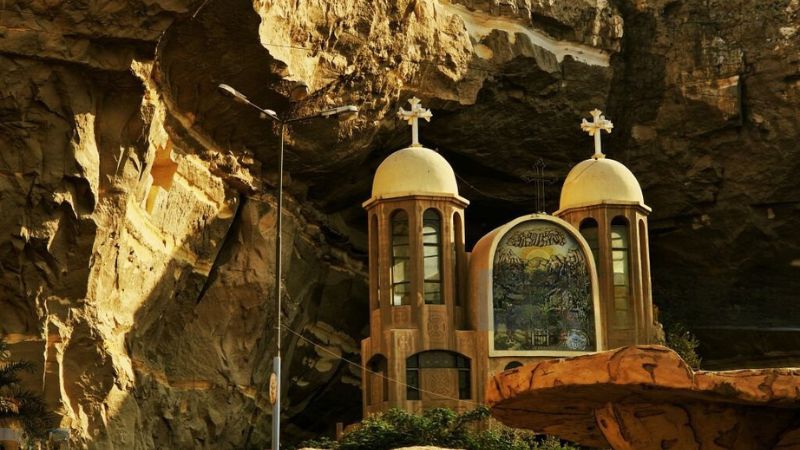 A church with twin domes set against a rocky cliff face, decorated with intricate carvings and religious symbols