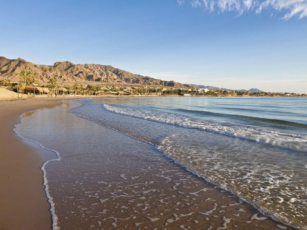 A pristine sandy beach with gentle waves, set against a backdrop of mountains and clear blue skies