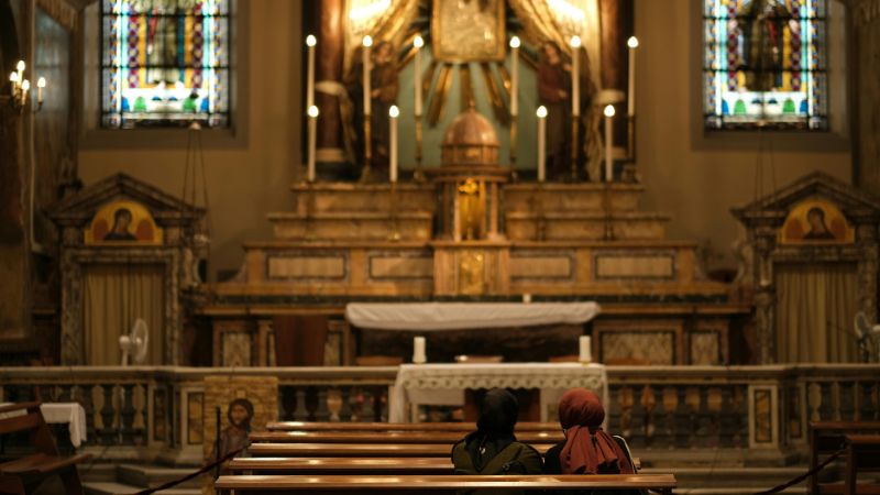 Two people seated in prayer facing a grand altar in a church with glowing candles and stained glass