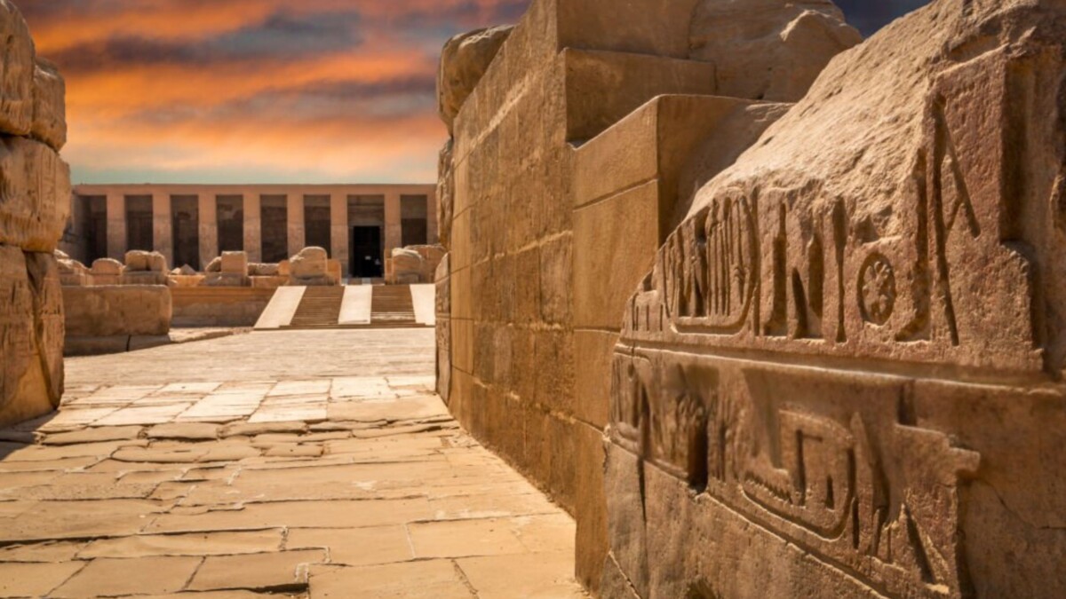 Outer courtyard of the Temple of Hathor in Dendera, featuring sandstone walls etched with hieroglyphs and a backdrop of a glowing sunset