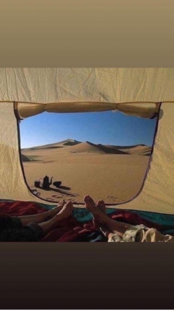 Desert landscape viewed from inside a tent with two people’s feet in the foreground