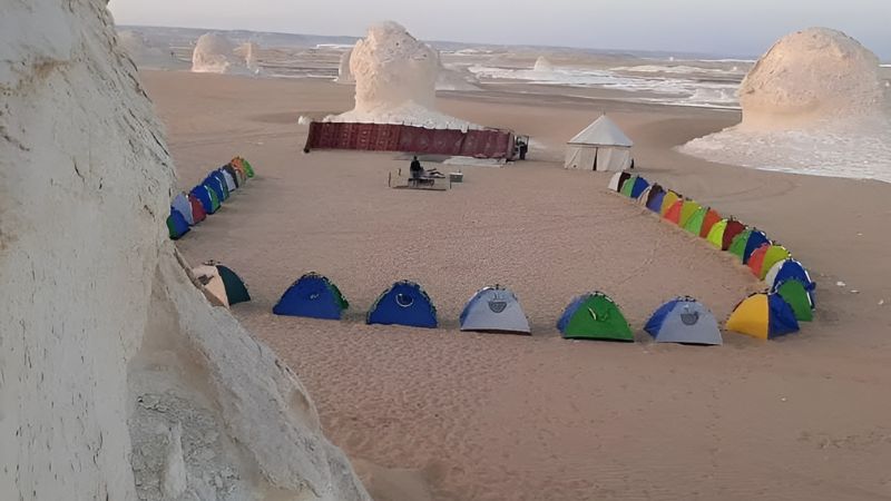 A serene desert camping scene in Egypt's White Desert, featuring tents set amidst unique white rock formations under a soft evening sky