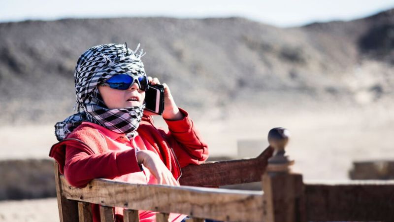 Tourist in desert attire talking on a mobile phone while seated outdoors