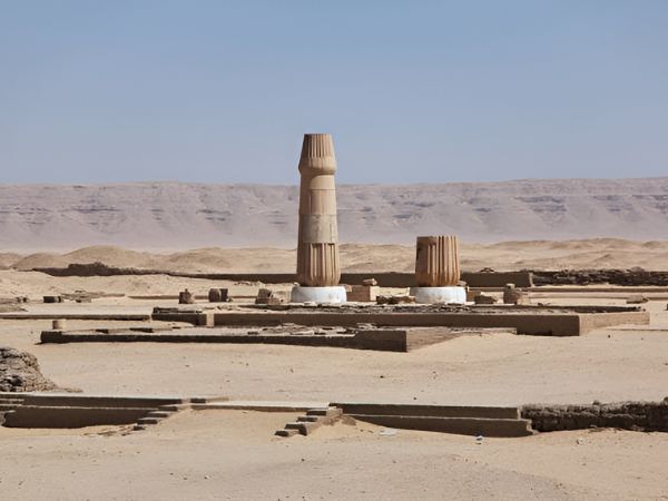 Two ancient columns standing in a desert archaeological site surrounded by vast sand dunes under a clear sky