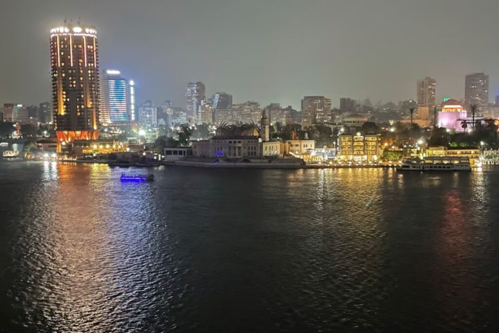 A luxurious dinner cruise boat sailing on the Nile River at night, with elegant lighting and reflections on the water.