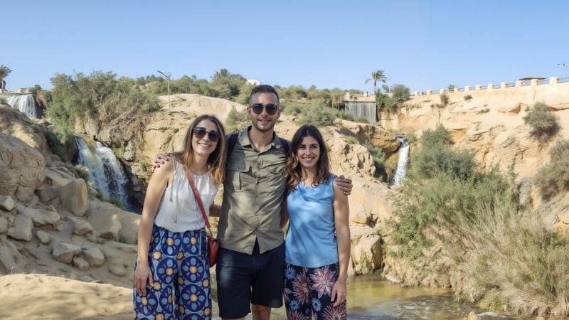 Travelers enjoying the refreshing waterfalls at an oasis in Egypt, surrounded by lush greenery and desert scenery