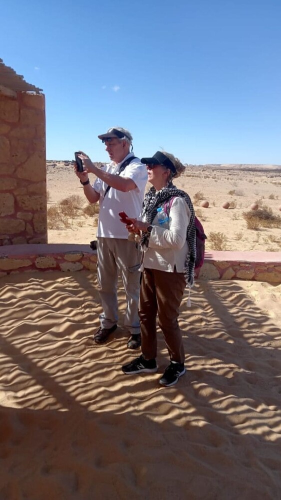 Tourists observing a water well in the desert surrounded by sand and hills