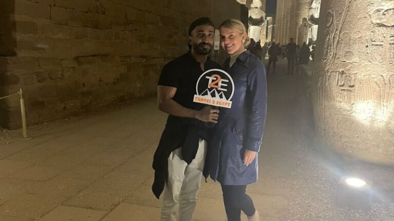 A man and woman posing with a "Travel & Egypt" sign in front of a historic temple at night