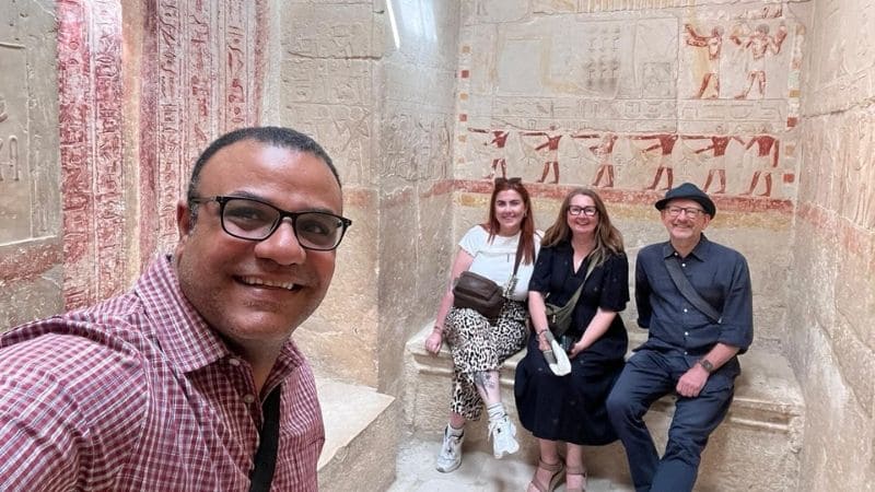 A visitor explores the interior of an ancient Egyptian tomb, with walls adorned with intricate hieroglyphs and colorful murals