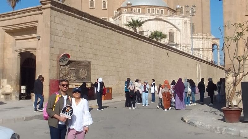 Tourists walking and sightseeing outside a historic building with stone walls and arches