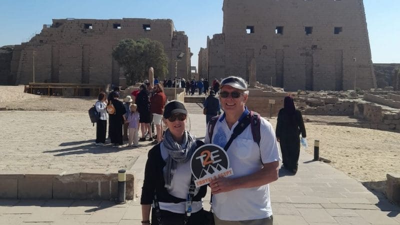 A couple holding a Travel 2 Egypt sign among towering columns in Karnak Temple, Luxor