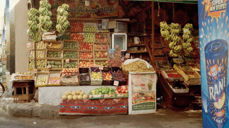 A colorful fruit stall displaying bananas, apples, oranges, and other fresh produce in an Egyptian market